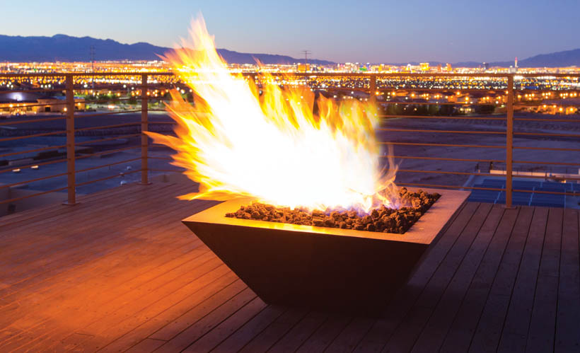 HPC fire outdoor copper gas fire pit high flame on patio overlooking the a city at sunset.